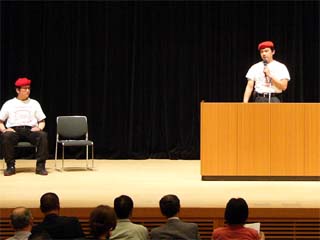 写真： トレードマークの赤いベレー帽と白いTシャツで講演するガーディアン・エンジェルスのメンバー